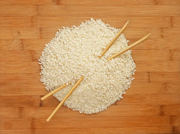 Raw rice and chopsticks on bamboo board