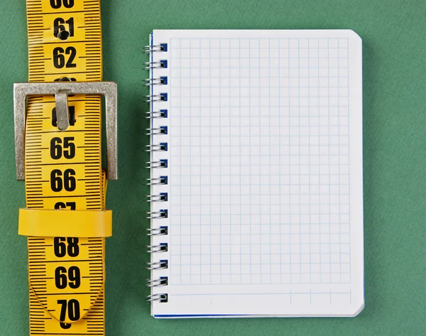 Meter belt slimming and notepad on the green background