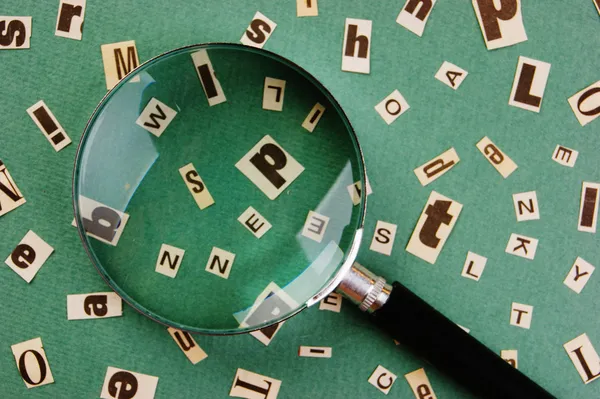 Letters cut from newspaper and magnifying glass on green background