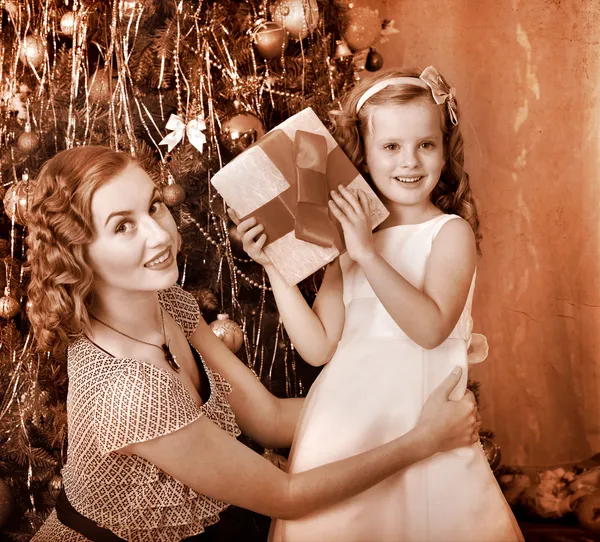 Kid with mother receiving gifts under Christmas tree.