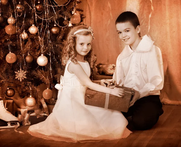 Children receiving gifts under Christmas tree.