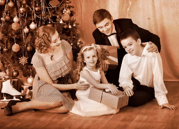Family with children receiving gifts under Christmas tree.