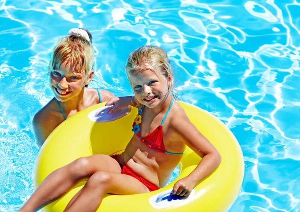 Children sitting on inflatable ring in water.