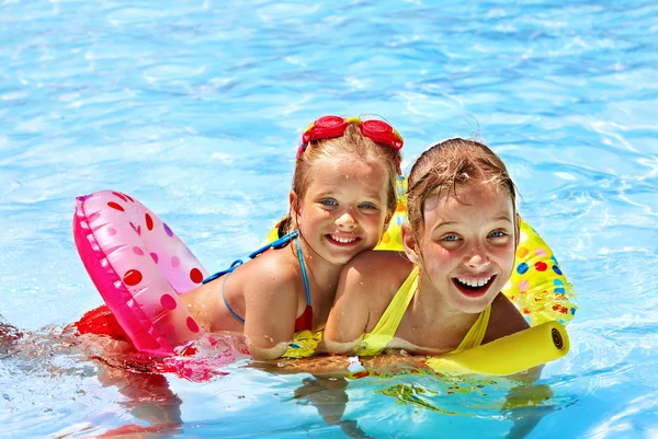Children sitting on inflatable ring in water.