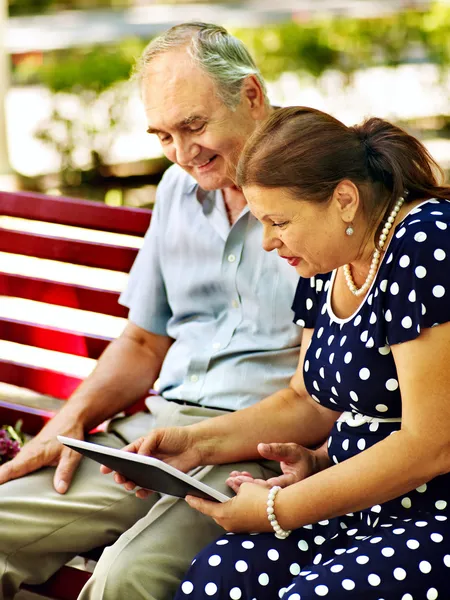 Old couple with tablet pc sit on bench .