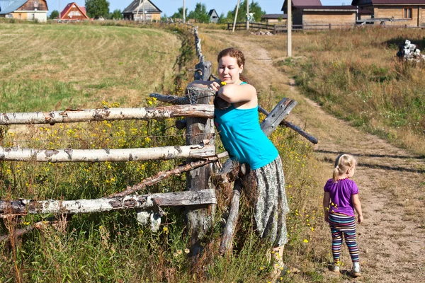 Young woman villager standing in front of wooden fence with her doughter