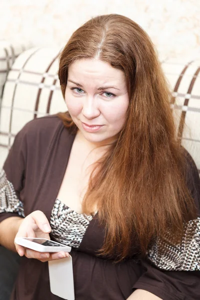 Portrait of Caucasian unhappy young woman with cellphone in domestic room