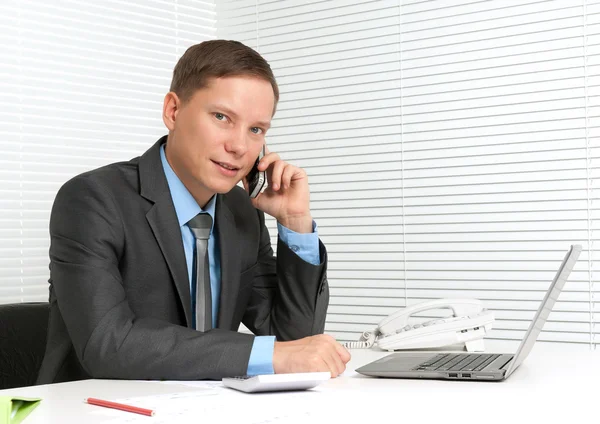 Cheerful young business man using mobile phone at desk