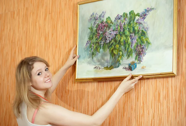 Woman hangs the picture on wall at home
