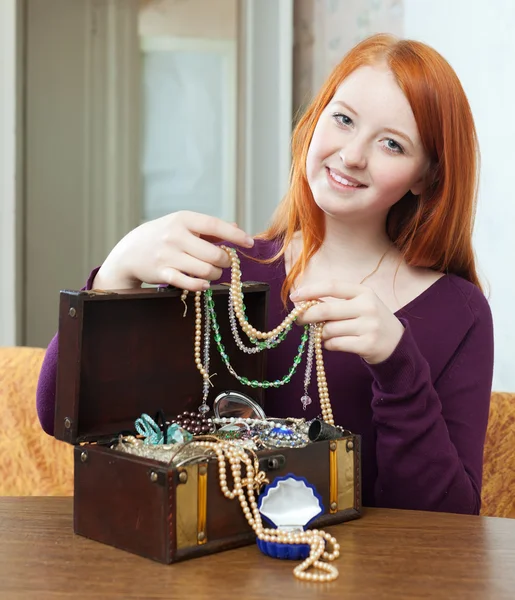 Red-headed girl looks jewelry in treasure chest