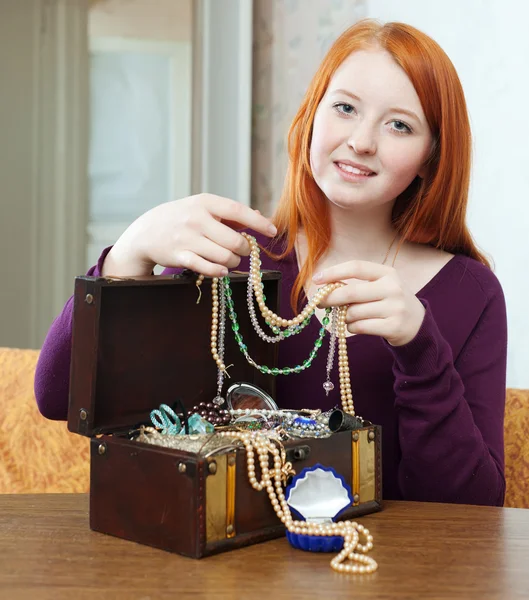 Red-headed girl looks jewelry in treasure chest