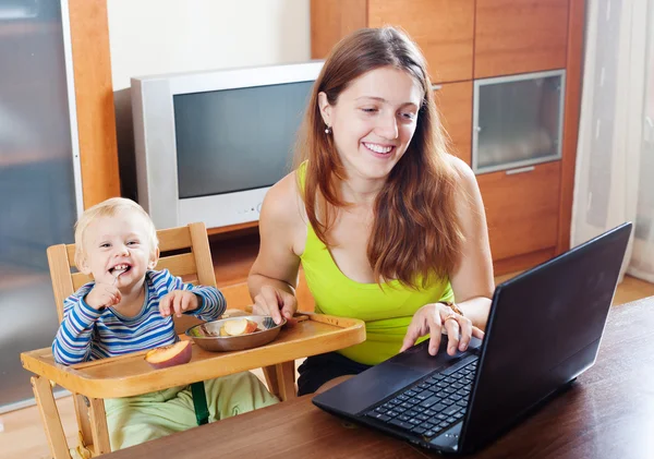 Happy young mother working with laptop and baby
