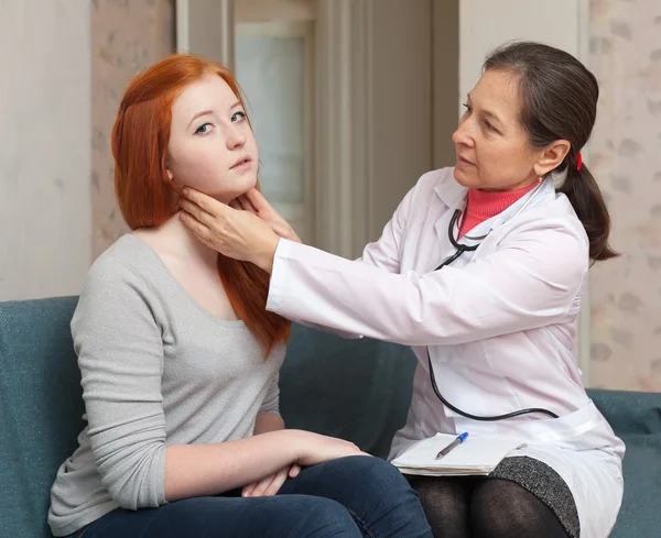 Mature physician palpates neck of teenager patient