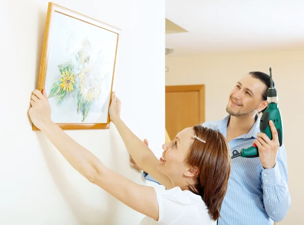 Middle-aged man and woman hanging art picture in frame