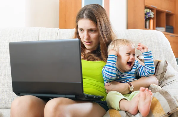 Young mother with crying baby working online