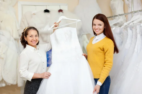 Shop assistant helps the bride in choosing dress