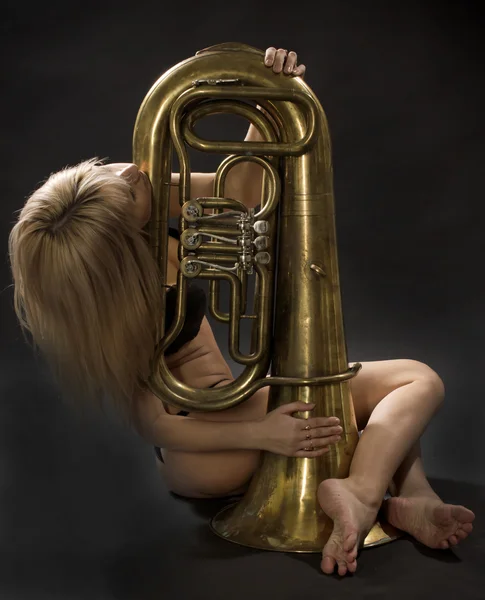 The girl sits with the big wind instrument on a black background