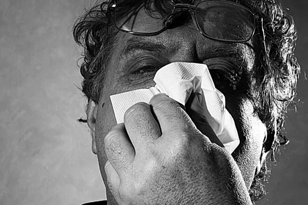 Middle-aged man blowing his nose into a tissue, black and white