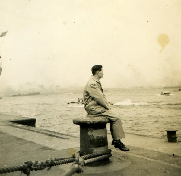 Man sitting on a bollard on the dock watching the sea