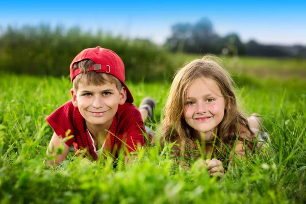 Cut boy and a girl are resting on the green grass in summer