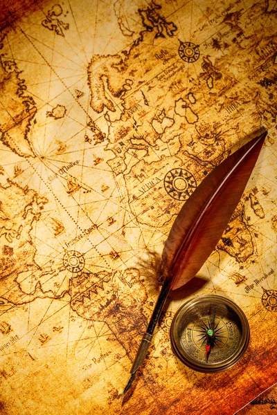 Vintage compass and goose quill pen lying on an old map.