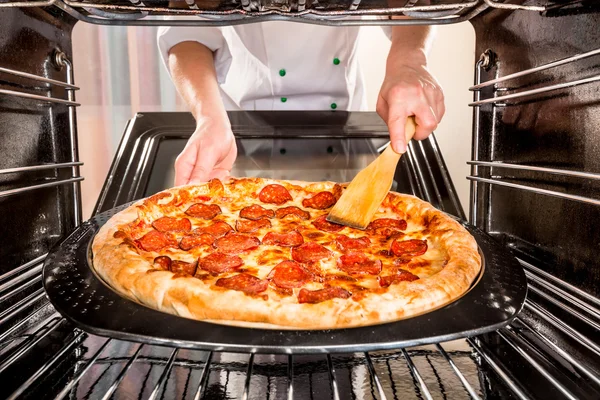 Chef cooking pizza in the oven.