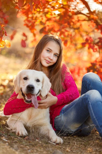 Portrait of Young girl sitting on the ground with her dog retriever in autumn scene