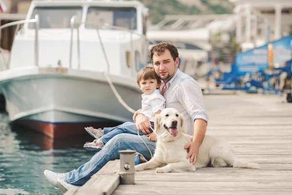 Father and son sits with dogs on a bench near the sea