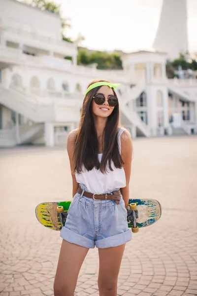 Beautiful and fashionable young woman posing with skateboard