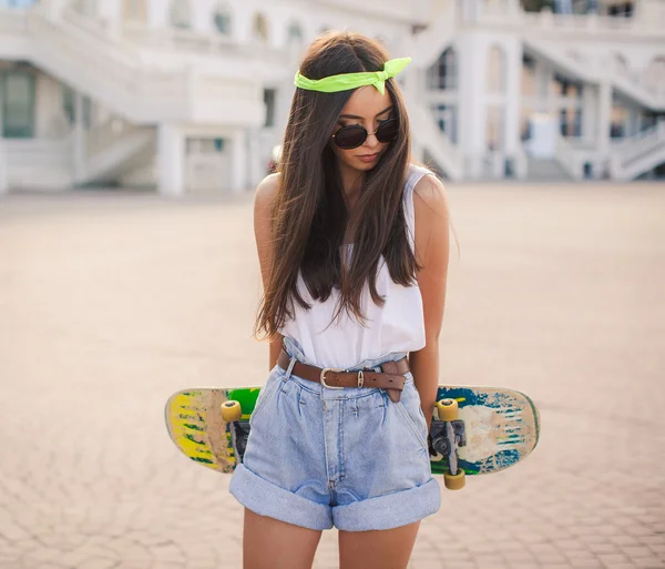 Beautiful and fashionable young woman posing with skateboard