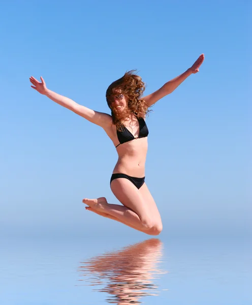 Young beautiful woman jumps against the sea