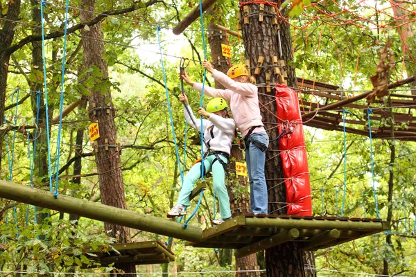 Mother and daughter in climbing equipment to overcome obstacles between high trees