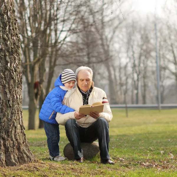 Grandfather and grandson reading a book outdoors