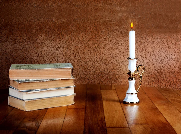 Old stack of books with candlestick and burning candle on the wo