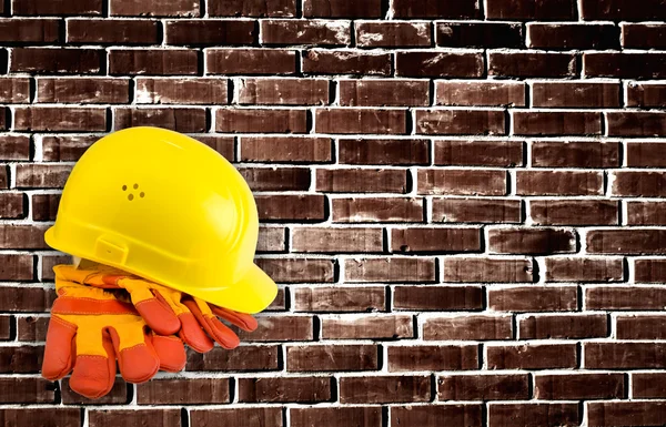 Yellow hard hat and protective gloves with grunge wall backgroun