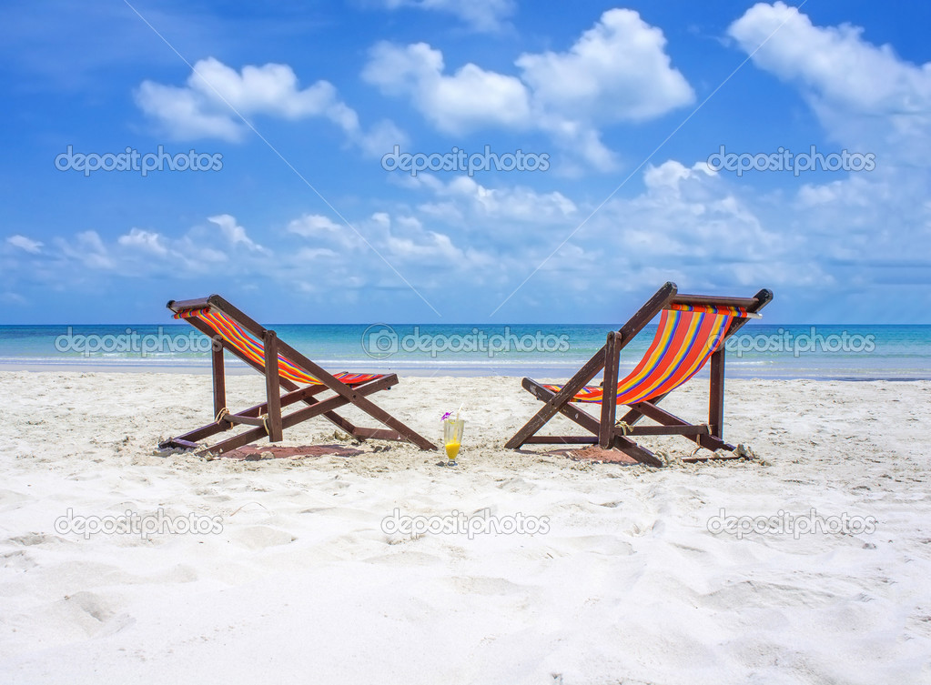 Zwei Liegestühle am weißen Sandstrand vor dem blauen Meer an einem