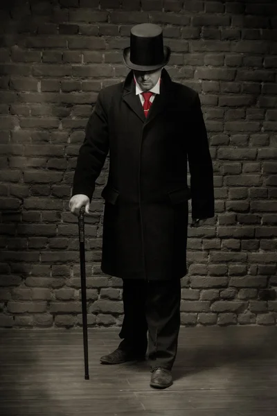 Man in the black coat, top hat and in a red tie