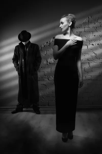 Woman in a long black dress and a man in a raincoat and hat