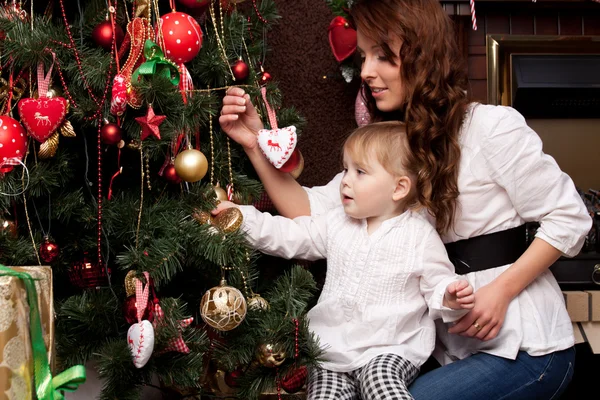 Happy mother decorating christmas tree with her baby