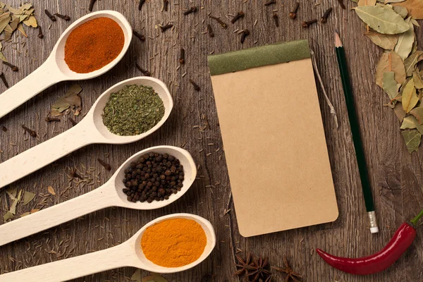 Peppers, spices in spoons, notebook and pencil