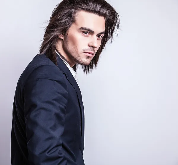 Elegant young handsome long-haired man in costume. Studio fashion portrait.