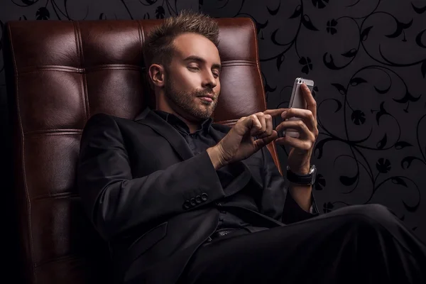 Handsome young man in dark suit relaxing on luxury sofa.