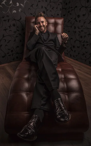 Handsome young business man in dark suit relaxing on luxury sofa.