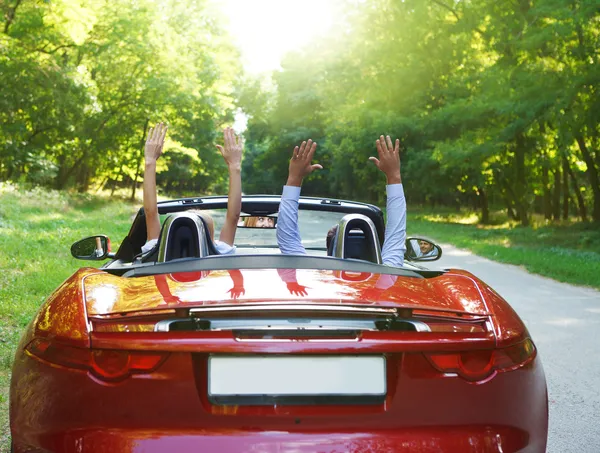 Happy free couple driving in red retro car cheering joyful with