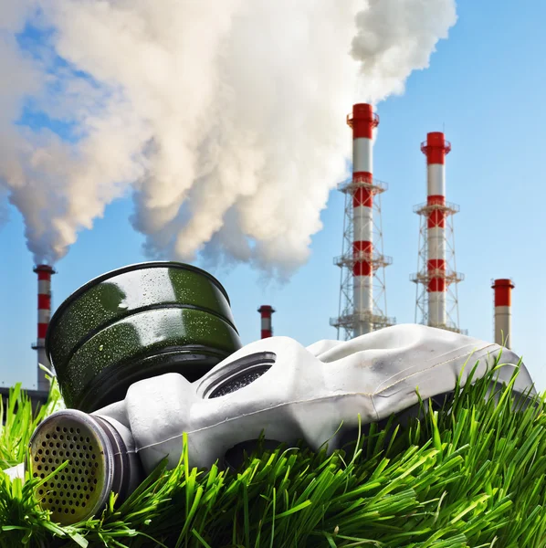 Gas mask on a green grass on a background of smoking chimneys