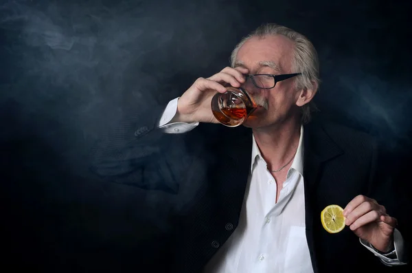 The elderly man with a glass of whisky on black background