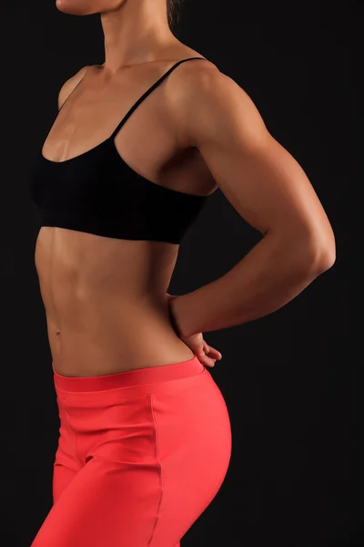 Muscular female body against black background.