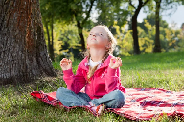 Little girl relaxing in yoga pose on grass in a park