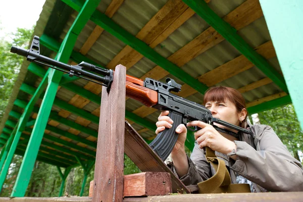 Young woman aiming at a target and shooting an automatic rifle f