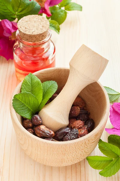 Essential oil in glass bottle, dried rose-hip berries and rose h